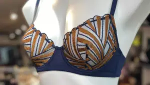 Close-up of a navy blue bra with intricate gold and white embroidered patterns in a bold geometric design, displayed on a mannequin in a softly lit boutique.