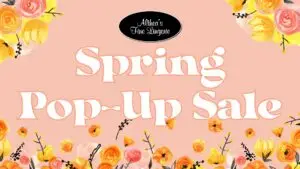 Promotional graphic for "Althea's Fine Lingerie Spring Pop-Up Sale." The background is a soft peach color with elegant white text outlined in a darker shade. Surrounding the text are watercolor-style floral illustrations featuring yellow, orange, and pink flowers with black stems and small accents. At the top, a black oval logo with white cursive text reads "Althea’s Fine Lingerie.