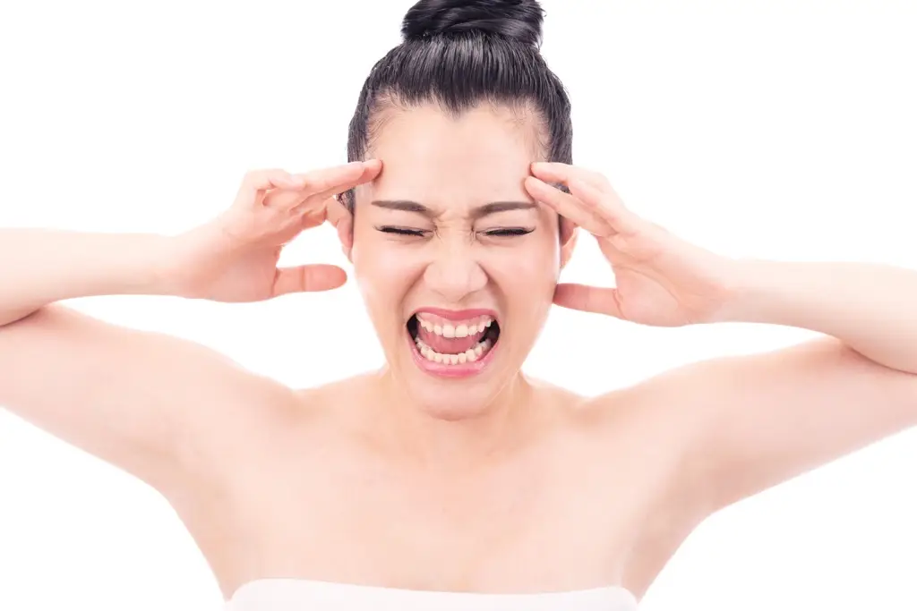 Woman holding her head in frustration, representing discomfort and stress from wearing a bra that doesn’t fit properly.