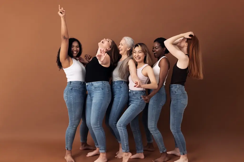Group of women with different body types smiling and dancing together, representing confidence and comfort after finding bras that fit well.