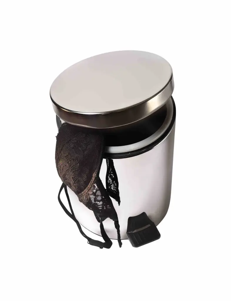 image of a black bra handing out of a trash can. It has been discarded because it is worn out.